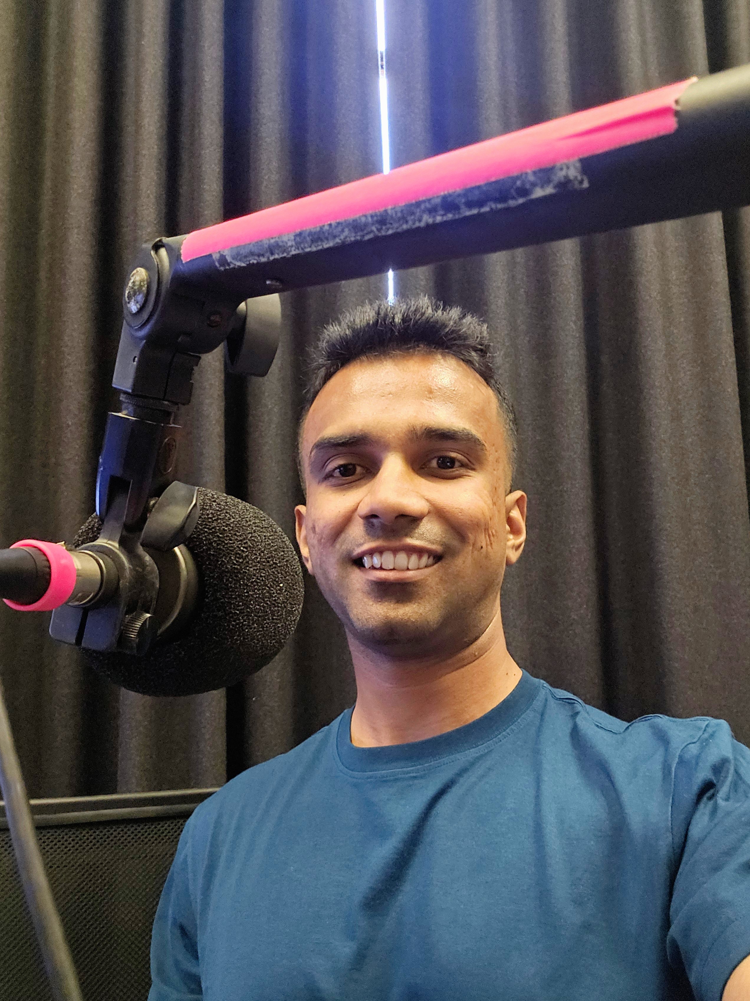 Hari smiling beside a podcast microphone